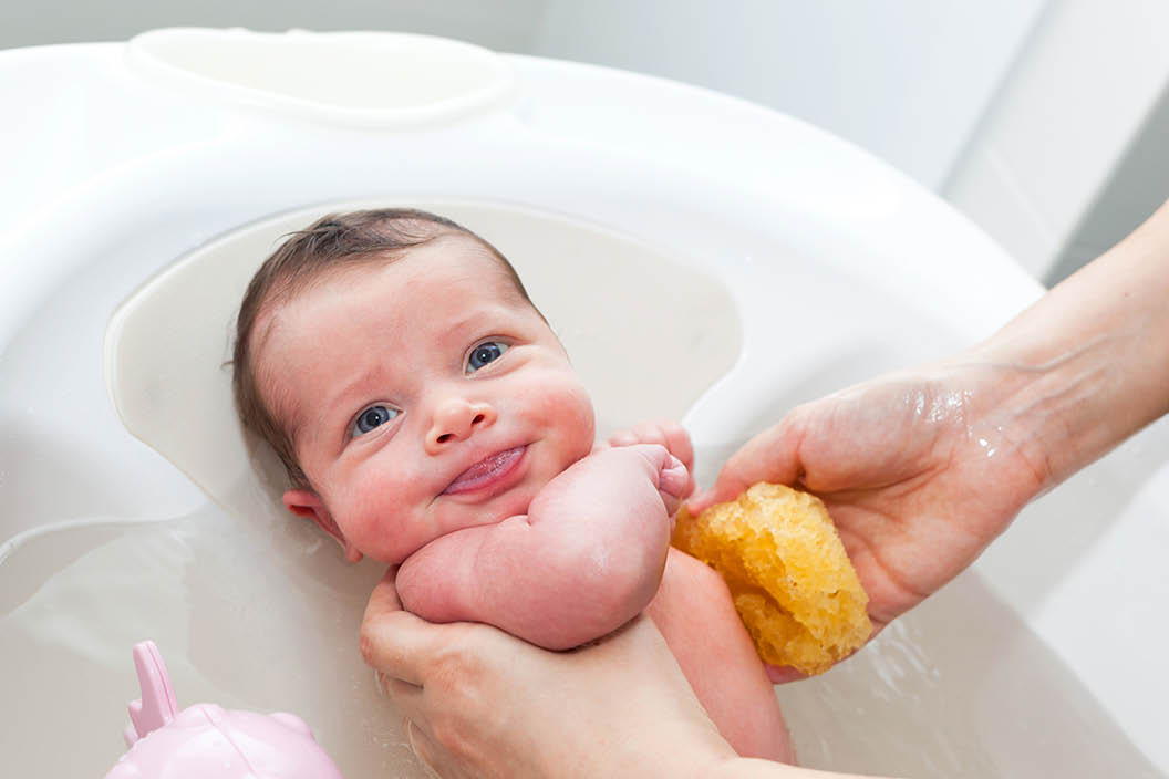 First bath of newborn baby girl.The mom washes the baby with natural sponge.