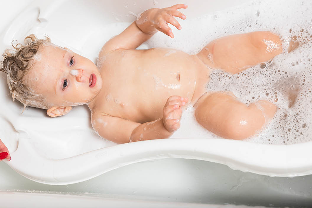 Little pretty wet baby boy in bath room lying on white background, horizontal picture.