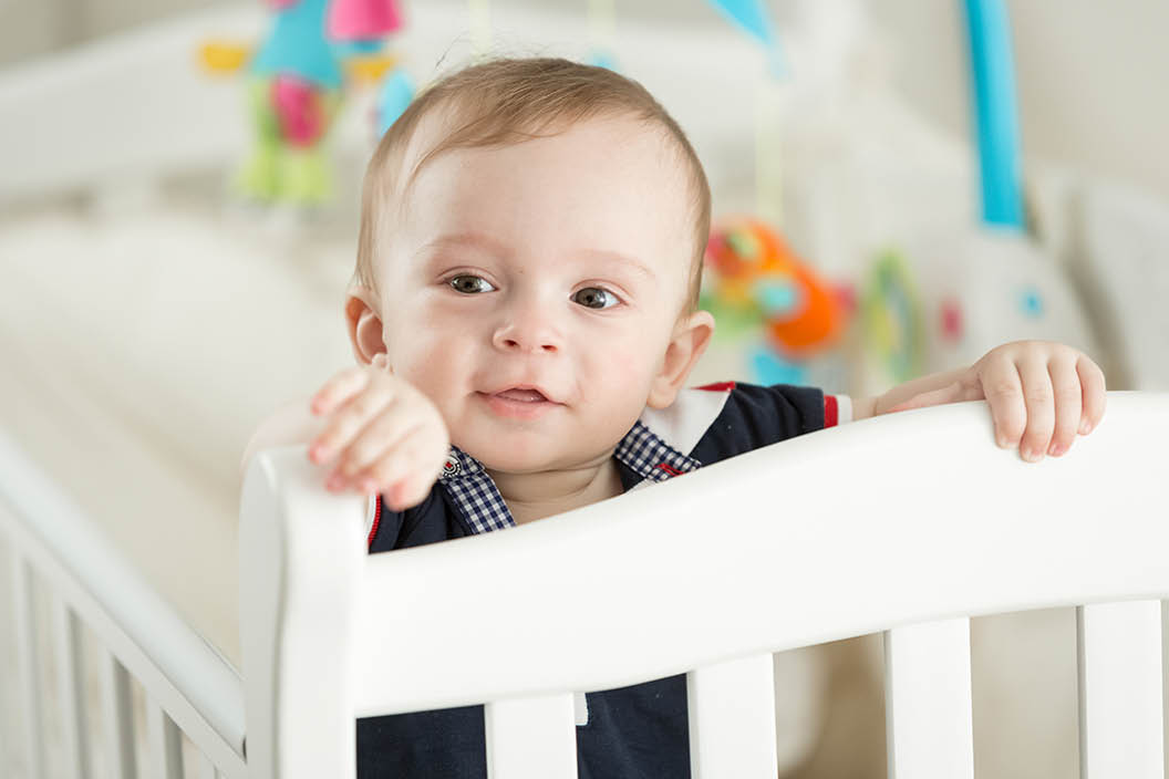 Portrait of 9 month old boy teething and posing in white cradle